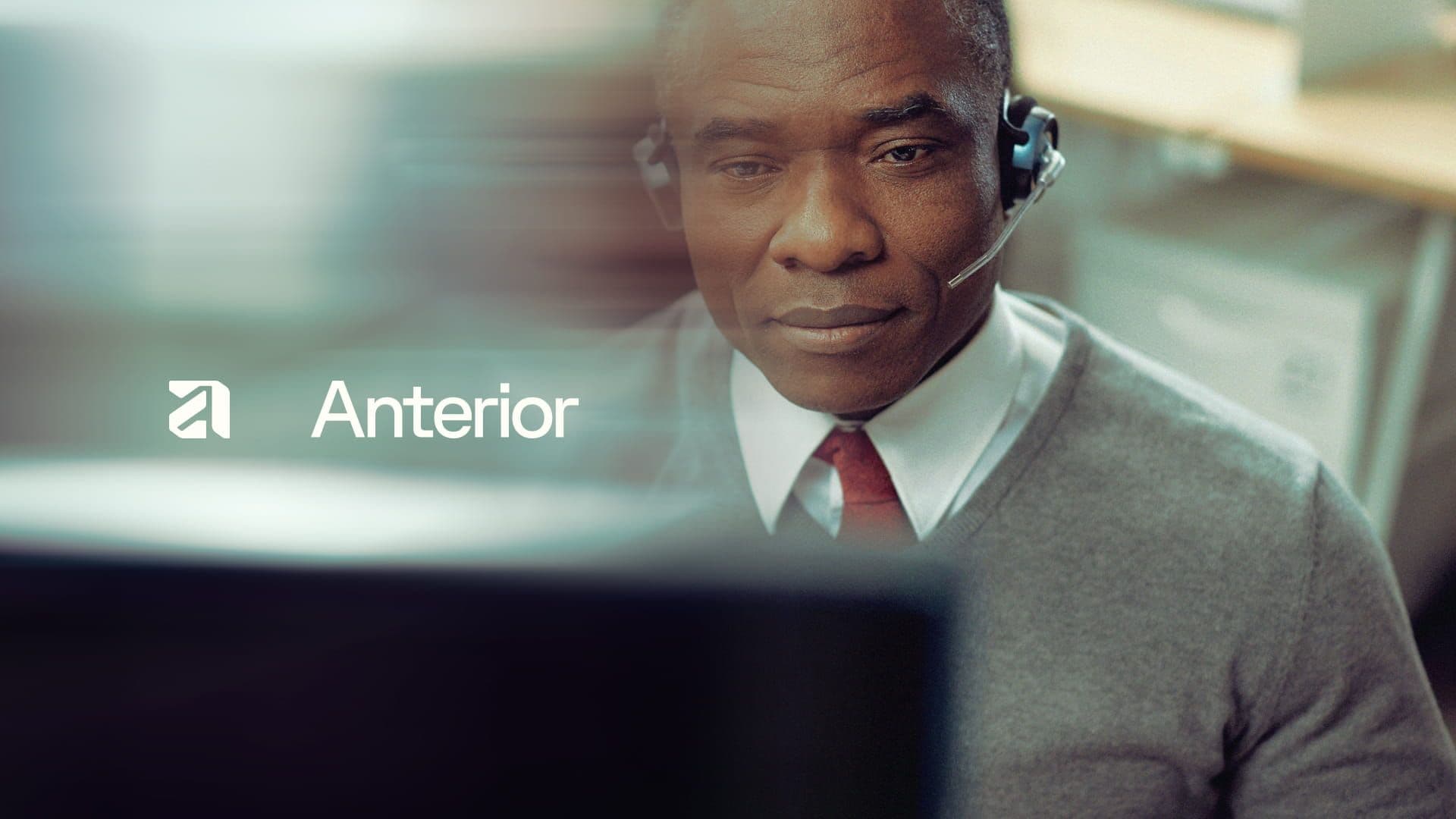 Healthcare professional wearing a headset, attentively engaging at a computer, symbolizing Anterior’s support for health plans committed to improving care for patients and providers. Anterior logo overlaid on a softly blurred office background.
